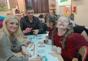 Dzieci razem z rodzicami kolorują zimowe obrazki.