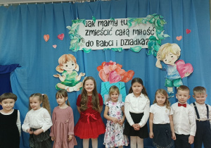 Dzieci z grupy 4-, 5- latków stoją na tle dekoracji.