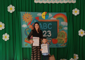 Jaś z dyplomem i nagrodą stoi w wychowawcą.