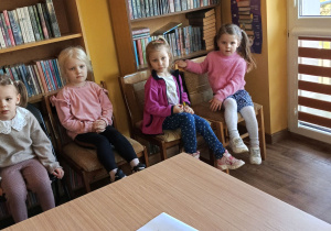 Dziewczynki siedzą na krzesłach przy regałach z książkami.