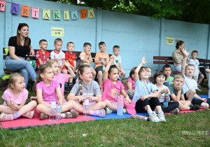 Grupa Jeżyków siedzi na kocach z wychowawcą.