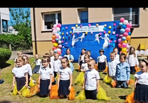 Dzieci z chustami klęczą na trawie.