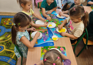 Przedszkolaki kolorują na żółto papierowe talerzyki.
