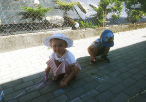 Dzieci rysują kredą po chodniku przed przedszkolem.