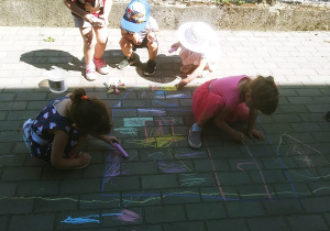 Dzieci rysują kredą po chodniku przed przedszkolem.