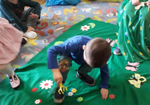Dzieci pomagają wiośnie układać kwiaty na łące.