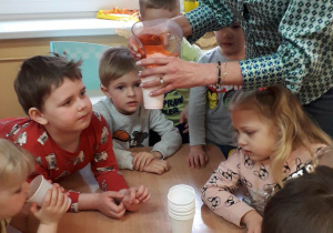 Dzieci piją sok nalewany przez panią Dorotkę.
