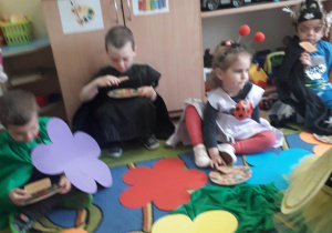Dzieci siedzą na kwiatowej łące i jedzą miodek.