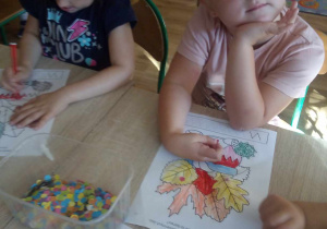 Dziewczynka nakleja kolorowe kółeczka na jesienne liście