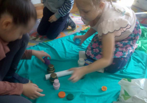 Dziewczynki układają motyla z papierowej rolki i plastikowych nakrętek