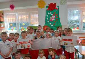 Grupa starszaków stoi na tle patriotycznej dekoracji.