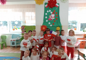 Grupa maluszków stoi na tle patriotycznej dekoracji.