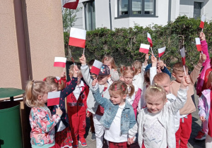 Dzieci idą z chorągiewkami wokół przedszkola.