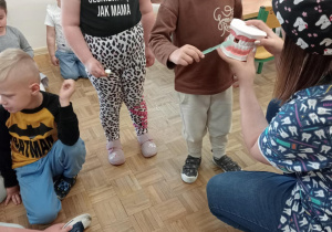 Pani pokazuje dzieciom szczotkowanie zębów na modelu sztucznej szczęki.