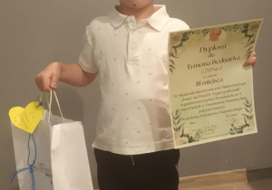 Nasz przedszkolak stoi z dyplomem wraz z nagrodą.