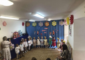 Grupa maluszków stoi na występie na tle dekoracji.