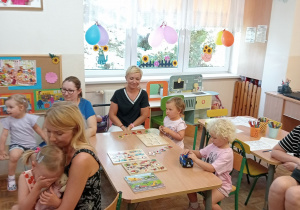 Dzieci wspólnie z rodzicami bawią się przy stolikach.