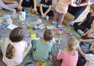 Dzieci siedzą na dywanie podczas zajęć o recyklingu.