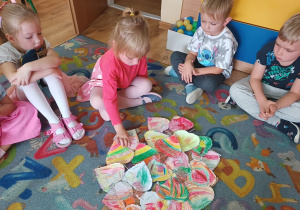 Dzieci siedzą na dywanie i przyklejają listki do drzewa.