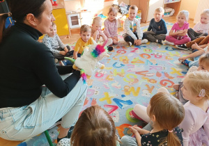 Dzieci siedzą w kole na dywanie i rozmawiają z panią psycholog.