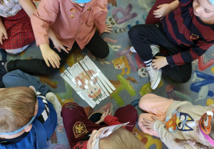 Przedszkolaki układają na dywanie obrazki z pociętych pasków.