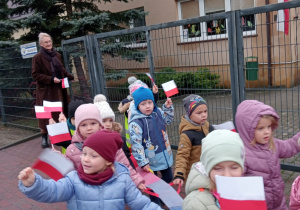 Najmłodsze przedszkolaki idą na spacer z choragiewkami.