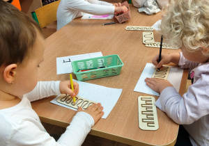 Dziewczynki piszą z wykorzystaniem tabliczek drewnianych.