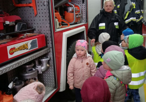 Przedszkolaki oglądają wyposażenie samochodu strażackiego.