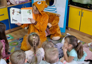 Pani bibliotekarka pokazuje przedszkolakom obrazki w książce.